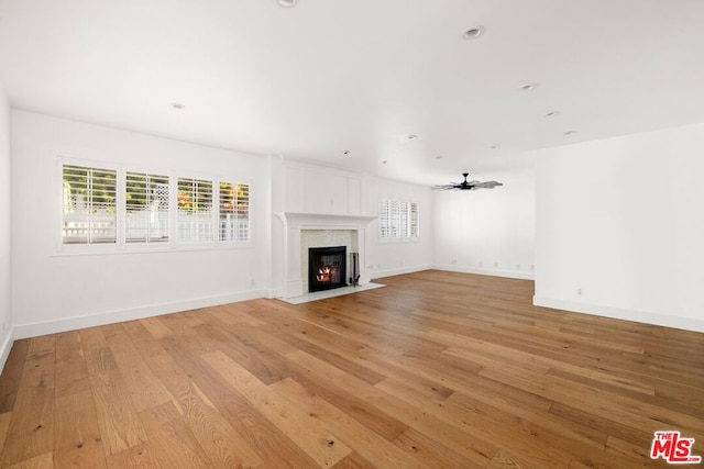 unfurnished living room featuring light wood-type flooring, ceiling fan, and a premium fireplace