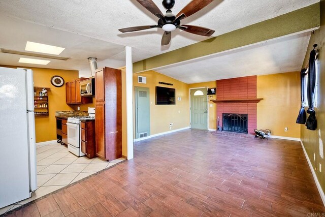 kitchen featuring ceiling fan, vaulted ceiling with beams, a textured ceiling, white appliances, and a fireplace