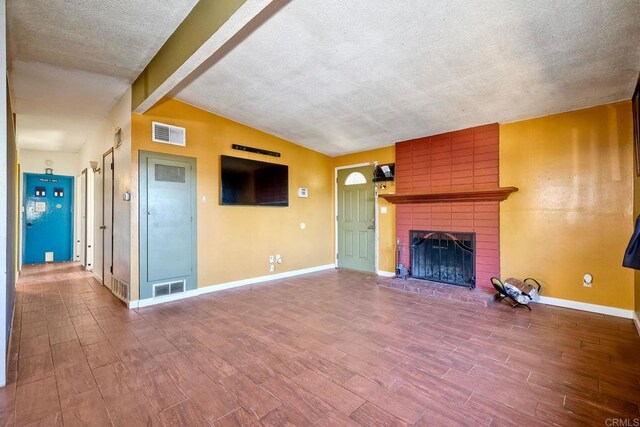 unfurnished living room featuring a textured ceiling, lofted ceiling with beams, and a brick fireplace