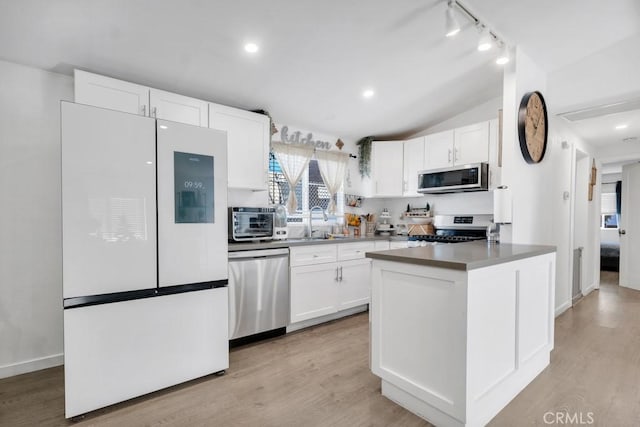 kitchen with lofted ceiling, white cabinets, stainless steel appliances, and light hardwood / wood-style floors