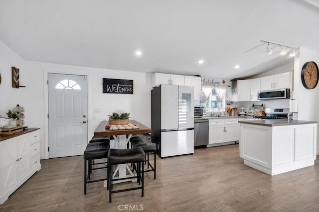 kitchen featuring appliances with stainless steel finishes, a center island, wood-type flooring, white cabinetry, and vaulted ceiling