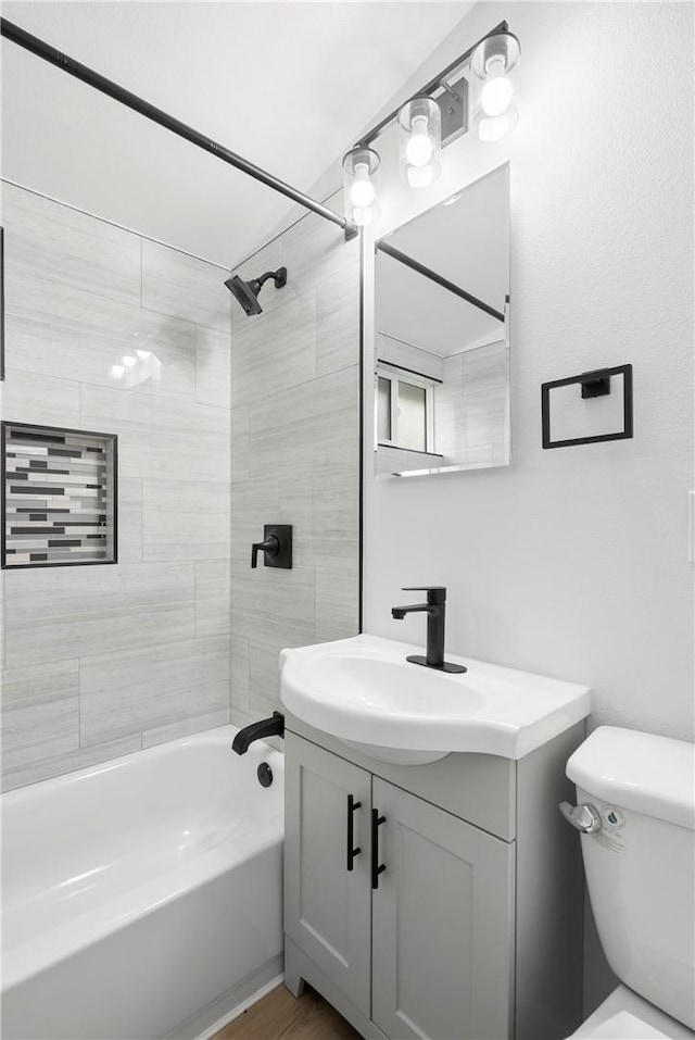 full bathroom featuring tiled shower / bath, vanity, and toilet