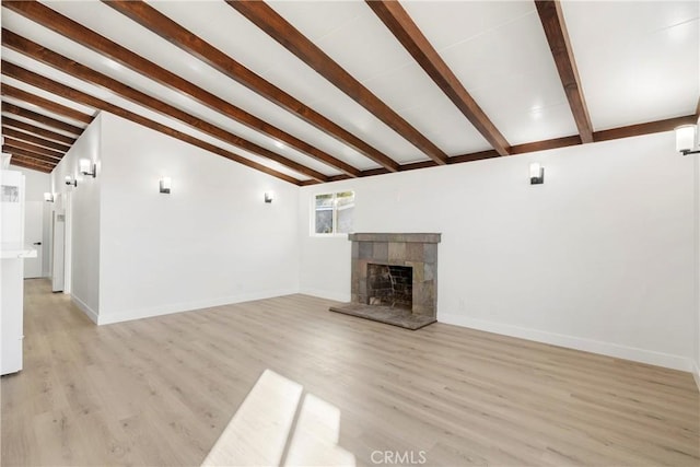 unfurnished living room with light wood-type flooring, lofted ceiling with beams, and a tiled fireplace