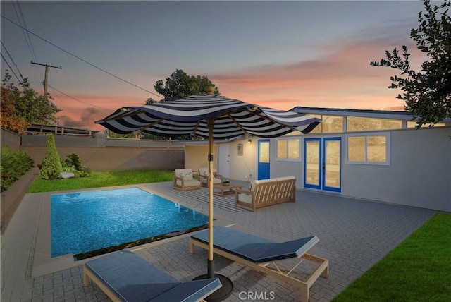 back house at dusk featuring outdoor lounge area, french doors, a fenced in pool, and a patio area