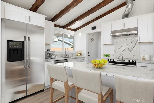 kitchen with stove, sink, stainless steel refrigerator with ice dispenser, light stone countertops, and white cabinetry