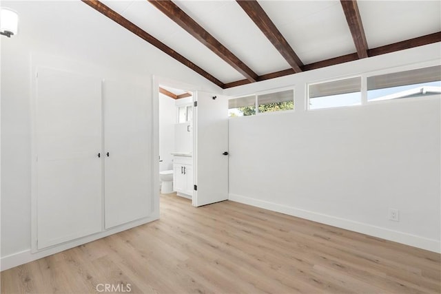 unfurnished bedroom with vaulted ceiling with beams, ensuite bath, and light wood-type flooring