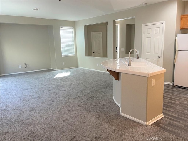 kitchen featuring sink, dark hardwood / wood-style floors, tile countertops, white fridge, and an island with sink