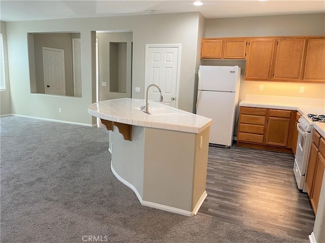 kitchen with tile counters, sink, dark wood-type flooring, white appliances, and a center island with sink