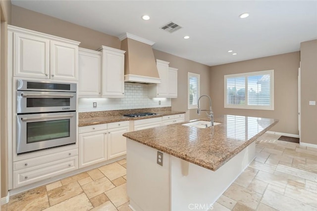 kitchen featuring custom exhaust hood, white cabinetry, a kitchen island with sink, and appliances with stainless steel finishes