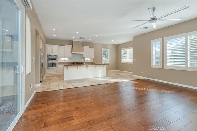 kitchen featuring white cabinetry, double oven, a kitchen bar, custom range hood, and light wood-type flooring