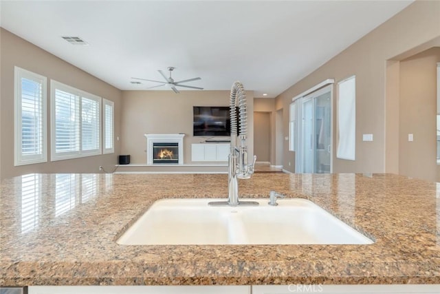 kitchen featuring ceiling fan, sink, and light stone counters