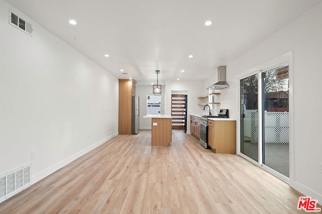 kitchen with appliances with stainless steel finishes, light wood-type flooring, wall chimney exhaust hood, pendant lighting, and a center island