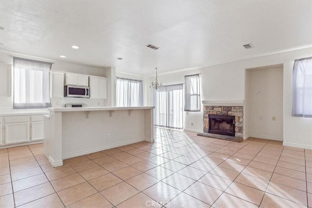 kitchen with a breakfast bar, a kitchen island, light tile patterned floors, white cabinets, and a stone fireplace