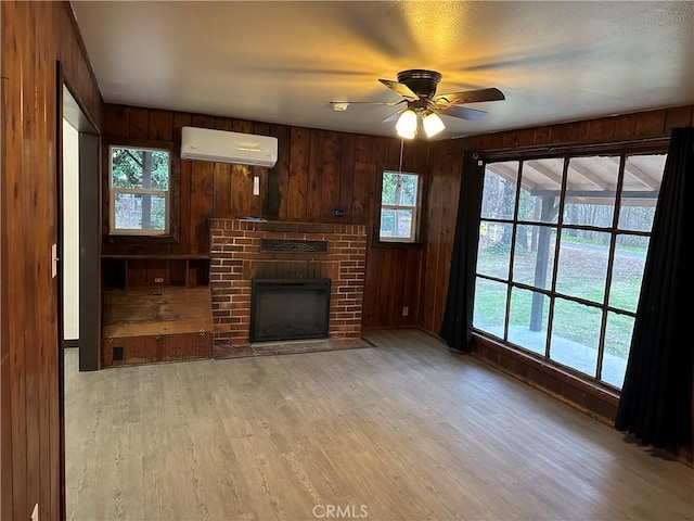 unfurnished living room featuring light hardwood / wood-style flooring, an AC wall unit, plenty of natural light, and wood walls