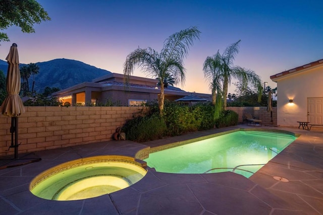 pool at dusk featuring a patio, an in ground hot tub, and a mountain view