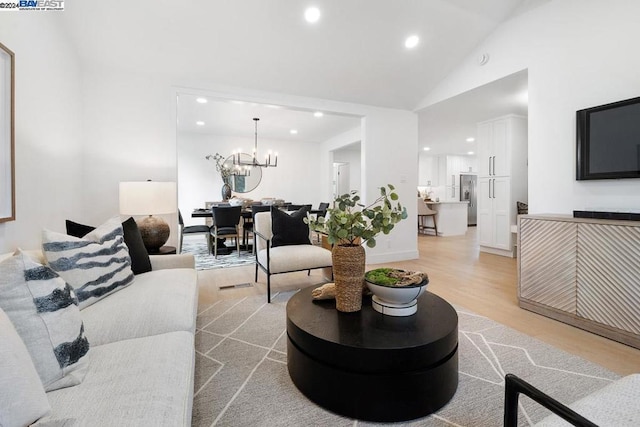 living room with a notable chandelier, light hardwood / wood-style floors, and vaulted ceiling