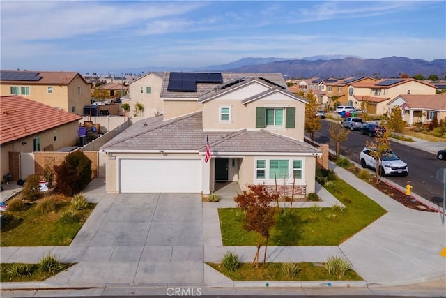 front facade with solar panels, a garage, a mountain view, and a front lawn