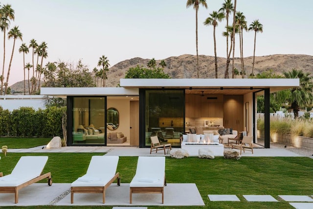 back house at dusk with an outdoor hangout area, a patio area, a mountain view, and a yard