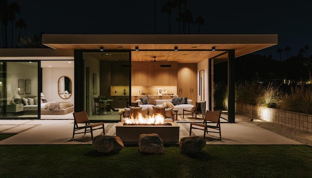 patio at night featuring ceiling fan and an outdoor living space with a fire pit