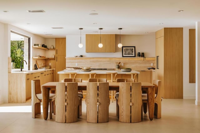 kitchen featuring light brown cabinetry, sink, hanging light fixtures, and tasteful backsplash