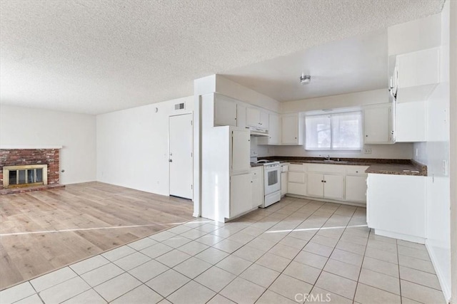 kitchen with a fireplace, white range with electric stovetop, sink, white cabinets, and light hardwood / wood-style floors