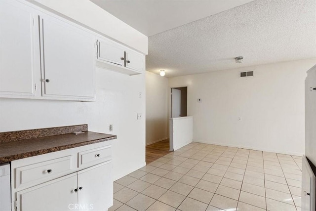 kitchen featuring a textured ceiling, white dishwasher, white cabinets, and light tile patterned floors