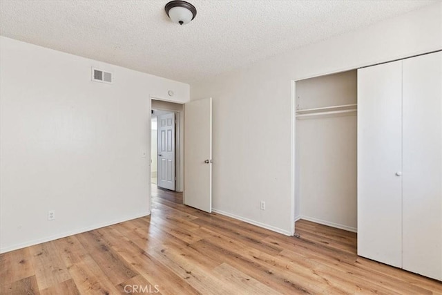 unfurnished bedroom with light wood-type flooring, a textured ceiling, and a closet