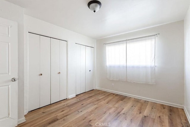 unfurnished bedroom with light hardwood / wood-style floors and multiple closets