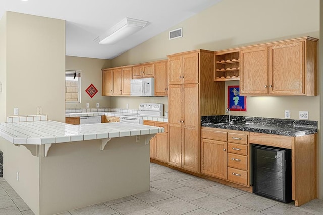 kitchen with white appliances, vaulted ceiling, tile countertops, wine cooler, and a breakfast bar area