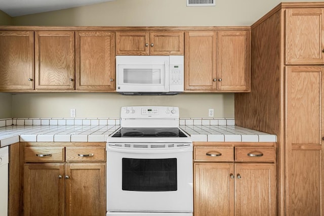 kitchen featuring white appliances, tile countertops, and vaulted ceiling