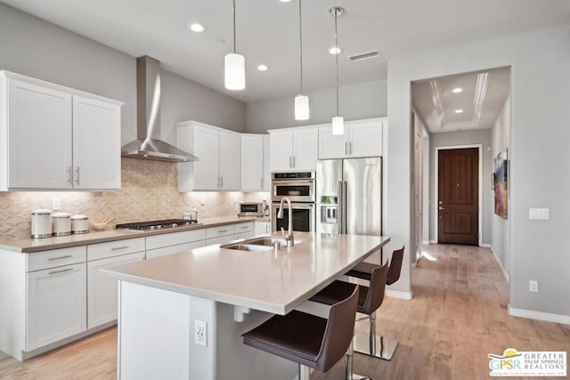 kitchen featuring white cabinets, a center island with sink, wall chimney exhaust hood, and appliances with stainless steel finishes