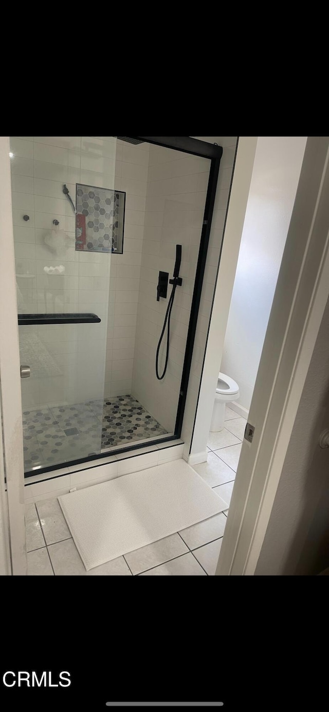 bathroom featuring toilet, tile patterned floors, and a shower with shower door