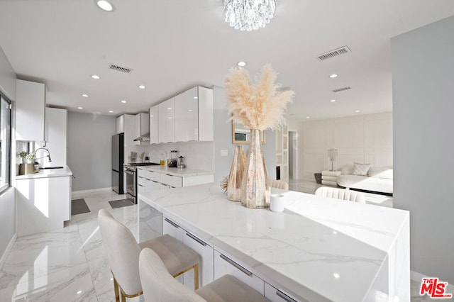 kitchen with white cabinets, a kitchen breakfast bar, a notable chandelier, light stone counters, and stainless steel appliances