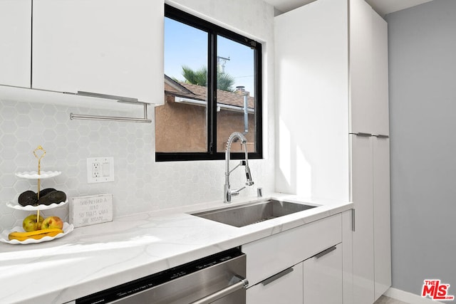 kitchen featuring white cabinets, decorative backsplash, light stone countertops, and sink