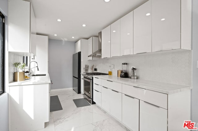 kitchen with light stone counters, stainless steel appliances, sink, wall chimney range hood, and white cabinets