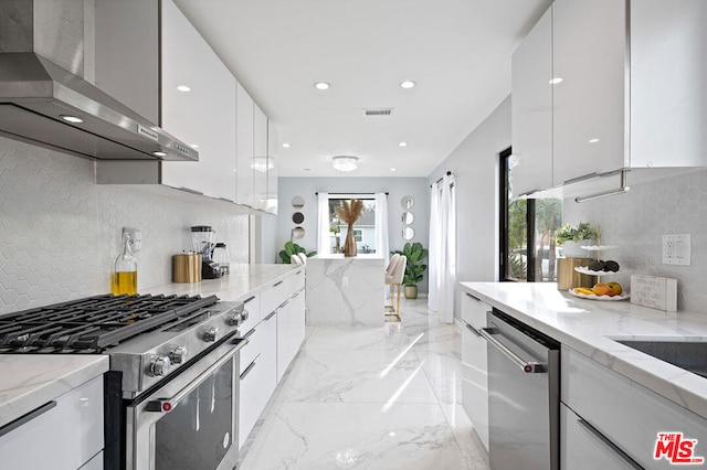 kitchen with decorative backsplash, appliances with stainless steel finishes, white cabinetry, and wall chimney range hood