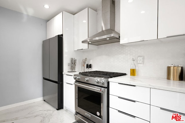 kitchen featuring wall chimney exhaust hood, decorative backsplash, light stone counters, white cabinetry, and stainless steel appliances