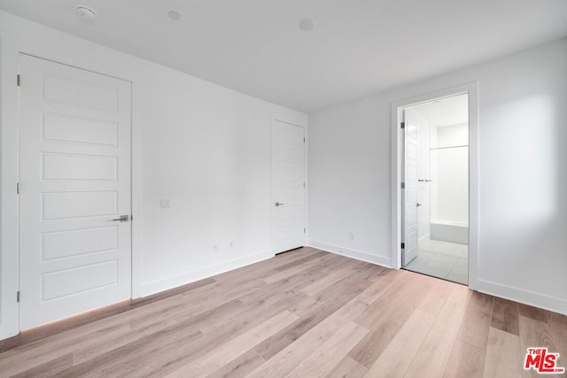 unfurnished bedroom with ensuite bath and light wood-type flooring