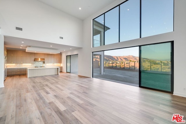 unfurnished living room with light hardwood / wood-style flooring, a mountain view, and a towering ceiling