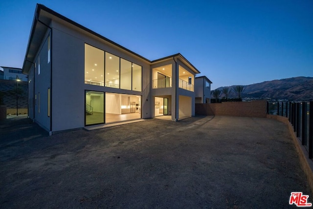 back house at dusk featuring a mountain view, a balcony, and a patio