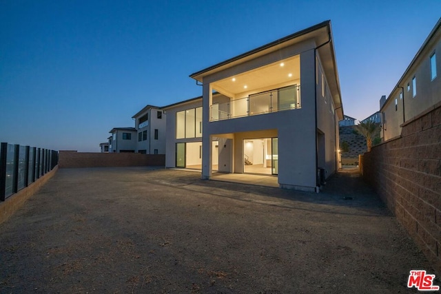 back house at dusk with a patio area and a balcony