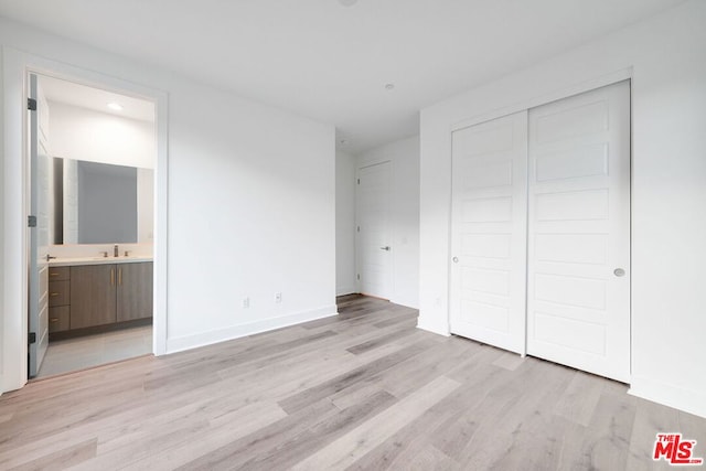 unfurnished bedroom featuring ensuite bath, light wood-type flooring, sink, and a closet