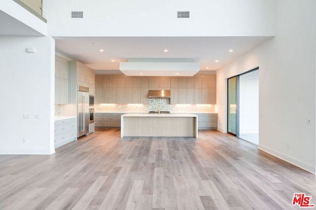 kitchen featuring ventilation hood, stainless steel appliances, tasteful backsplash, a kitchen island with sink, and light hardwood / wood-style flooring