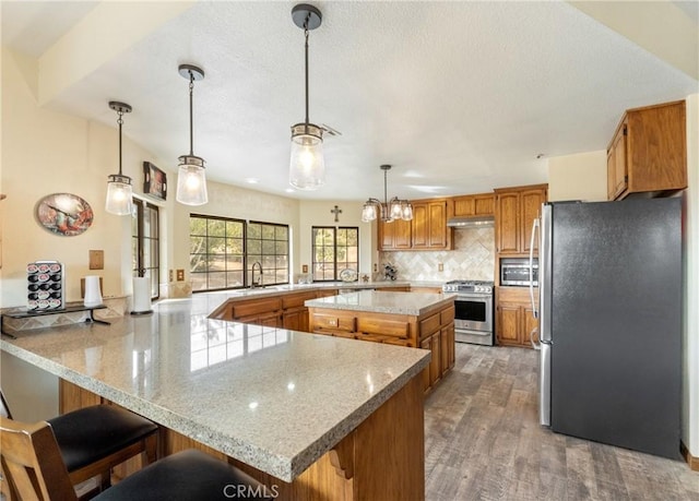 kitchen featuring hanging light fixtures, range hood, appliances with stainless steel finishes, dark hardwood / wood-style flooring, and kitchen peninsula