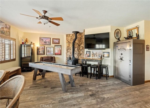 playroom featuring ceiling fan, wood-type flooring, and a wood stove