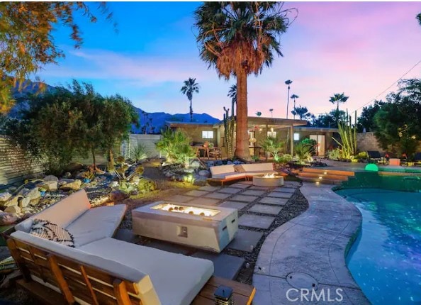 pool at dusk featuring a mountain view, a patio area, and an outdoor living space with a fire pit