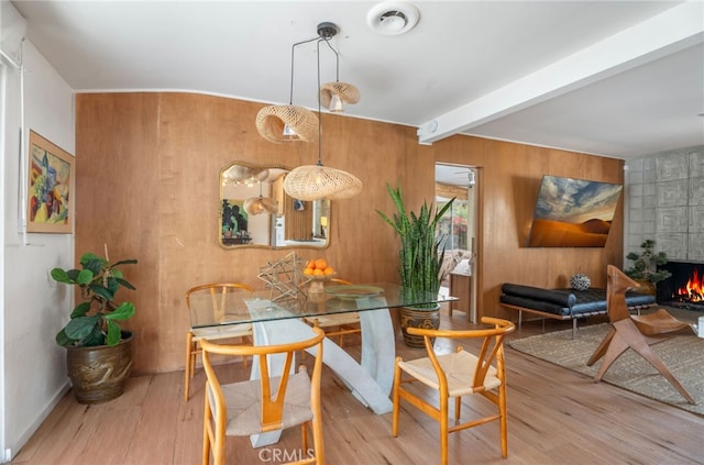 dining area with a fireplace, beamed ceiling, light hardwood / wood-style floors, and wooden walls