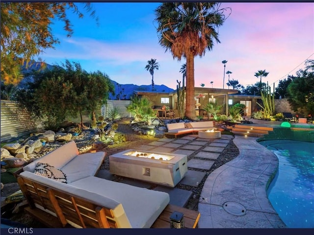 pool at dusk with a mountain view, a patio area, and an outdoor living space with a fire pit