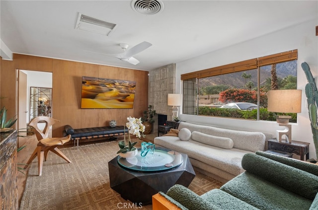 living room with ceiling fan, a fireplace, and wood walls