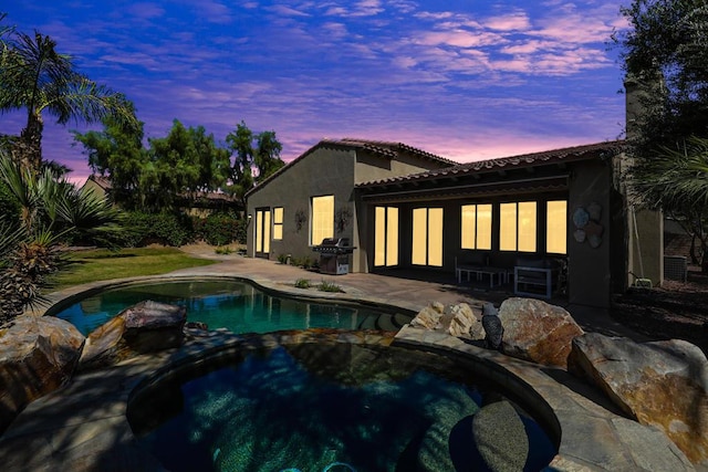 pool at dusk featuring a grill, an in ground hot tub, and a patio